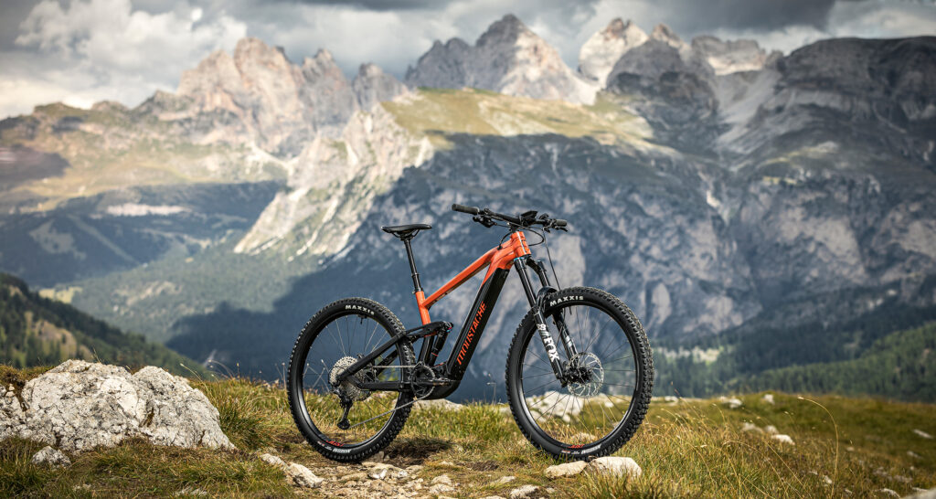 Ein Moustache Samedi Game E-MTB steht vor einem eindrucksvollen Bergpanorama.